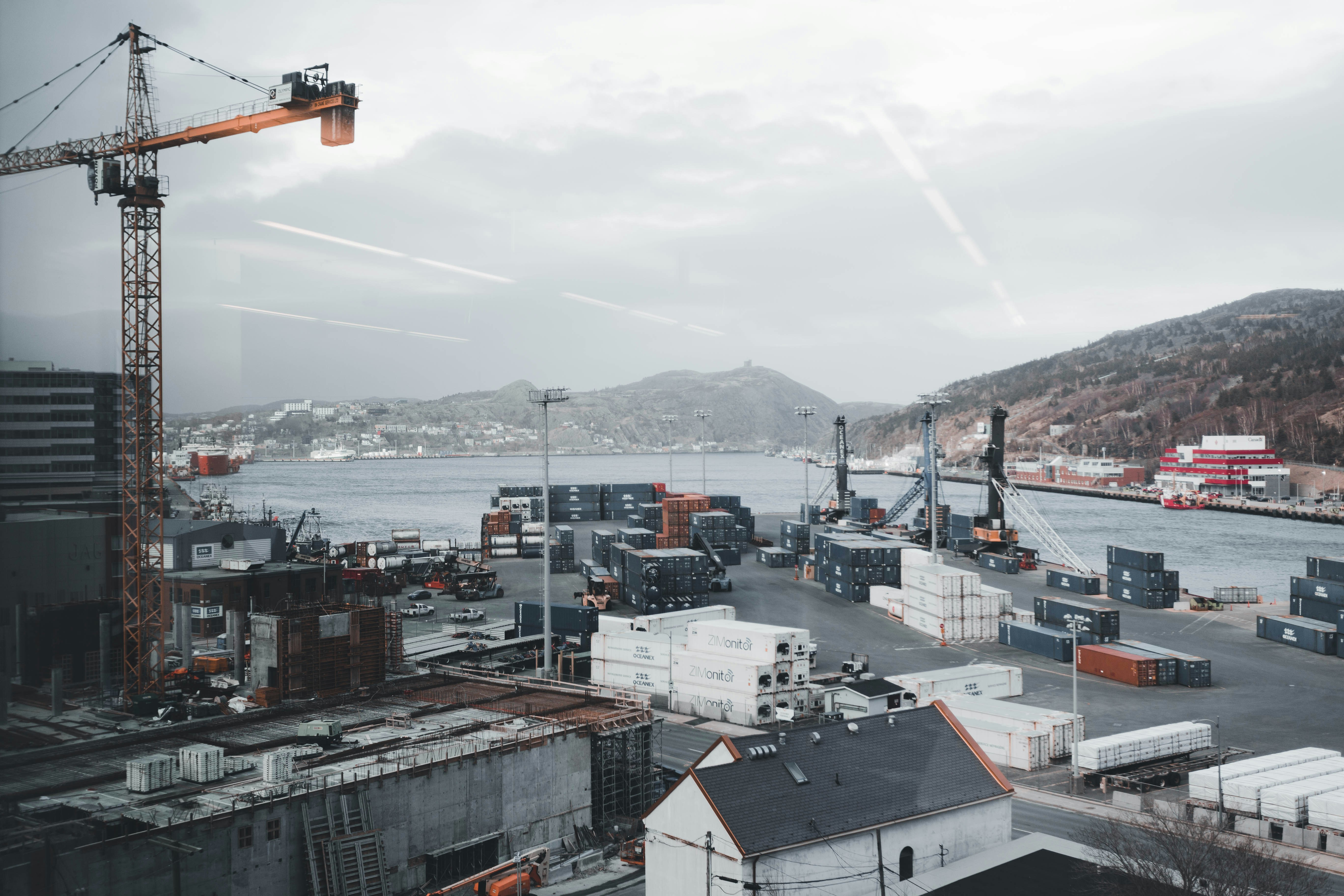 Industrial port at night with cranes and cargo ships under heavy overcast sky, dark steel, low-key lighting, deep shadows