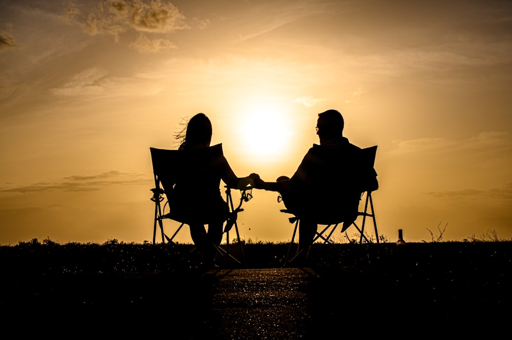 a man and woman sitting on a chair in front of a sunset
