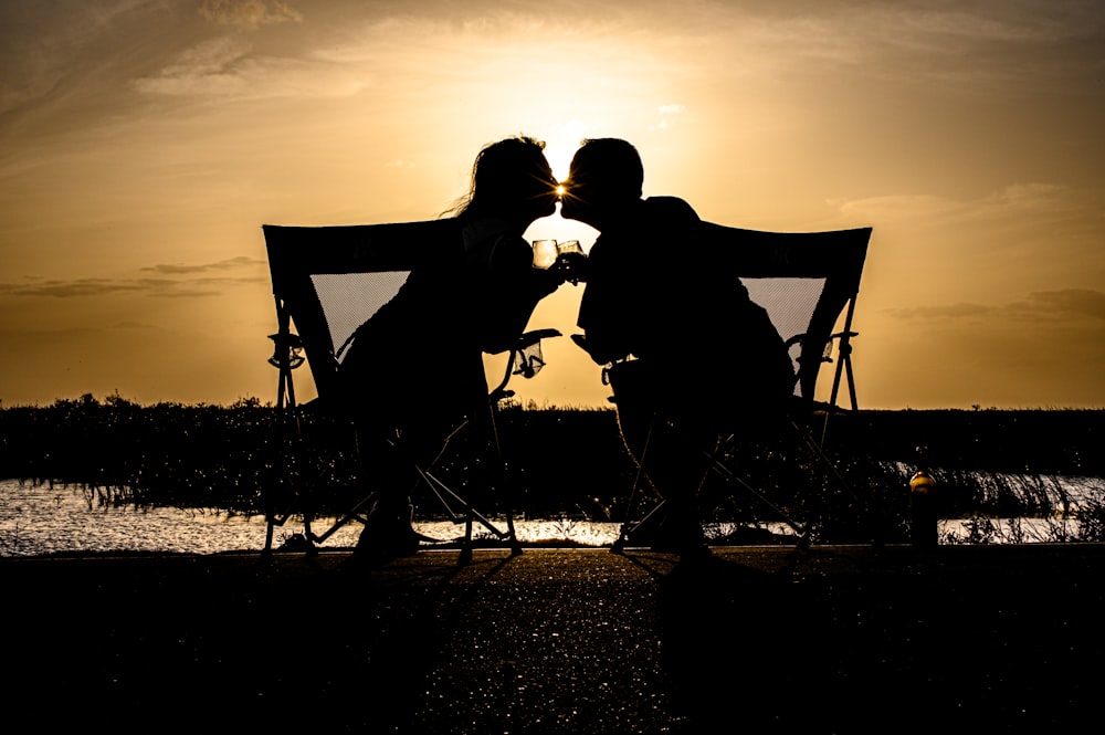 a couple of people sitting on a bench with a canopy and a sunset
