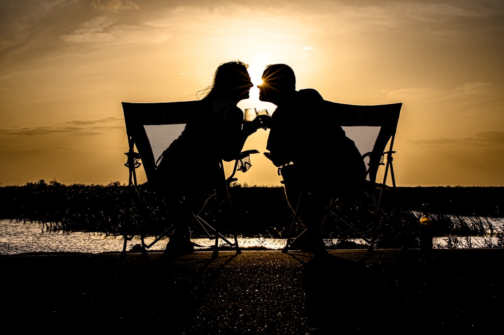 a couple of people sitting on a bench with a sunset in the background