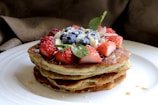 A stack of almond flour pancakes topped with fresh berries and a drizzle of honey on a wooden plate