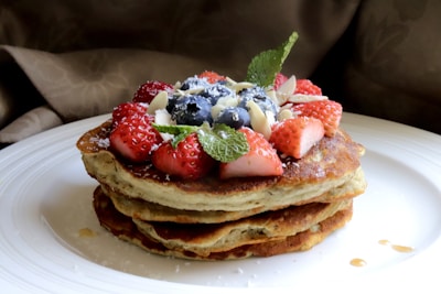 A stack of almond flour pancakes topped with fresh berries and a drizzle of honey on a wooden plate