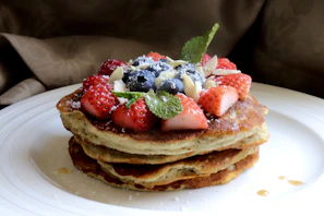 A stack of fluffy protein pancakes garnished with maple syrup and a sprig of mint on a wooden table.