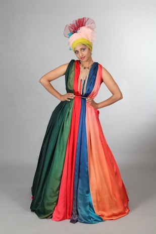 Regal Rhythm in a dramatic John Galliano-inspired gown with subtle rainbow accents under soft stage lighting.