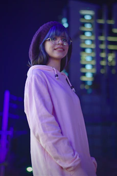 A smiling person wearing sleek eyeglasses, standing against a bright city backdrop.