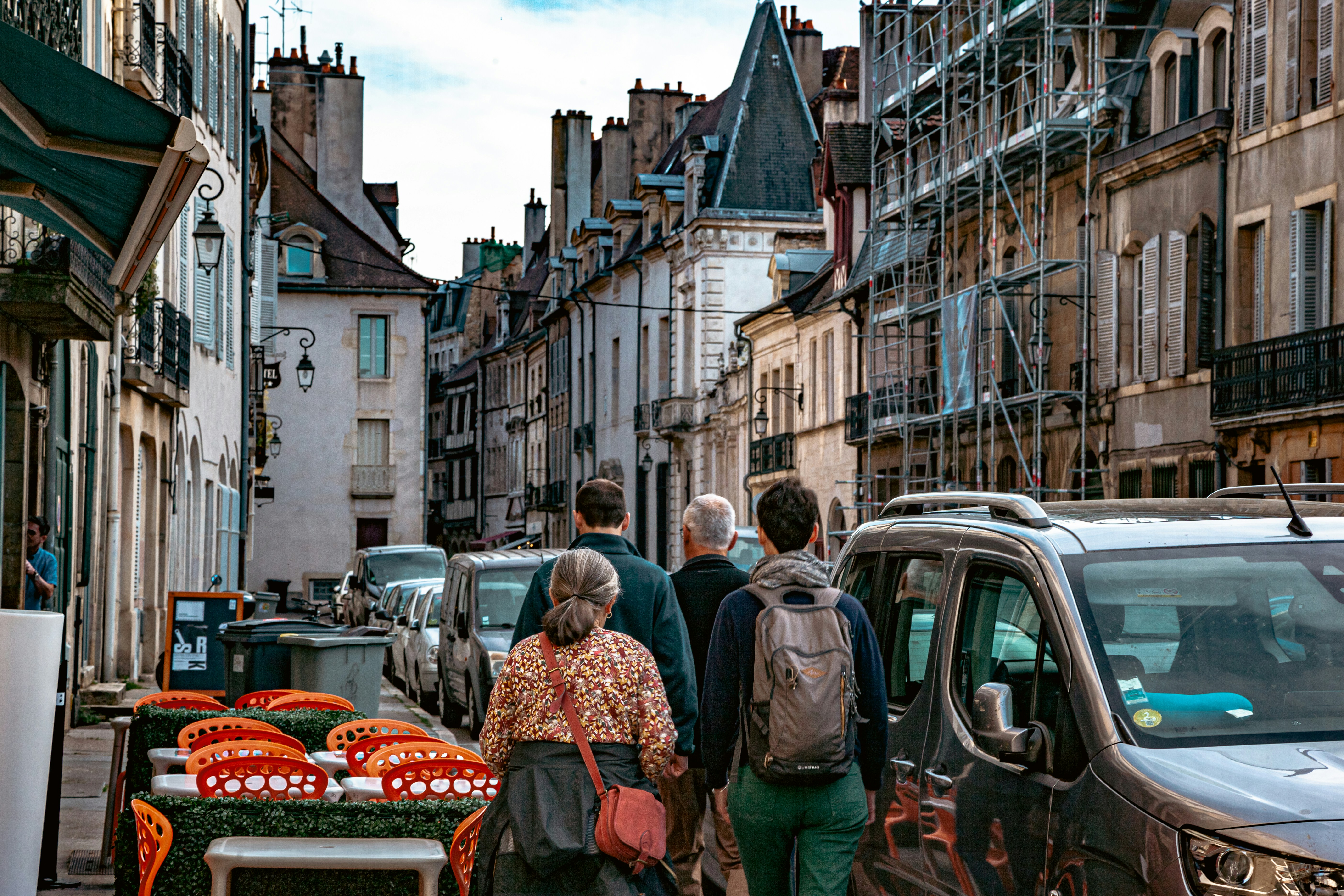 a group of people walking down a street lined with parked cars
