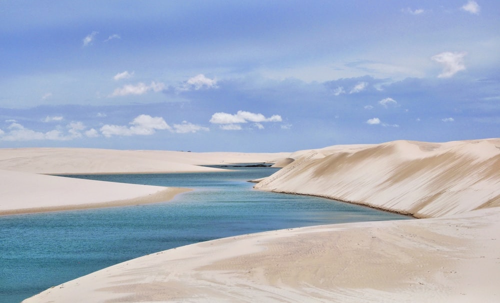 ein Sandstrand mit einem Gewässer im Hintergrund mit dem Nationalpark Lençóis Maranhenses im Hintergrund