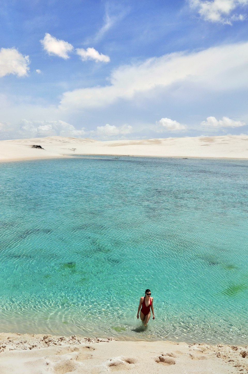 A person standing in the clear turquoise water of a lagoon at Lençóis Maranhenses, Brazil