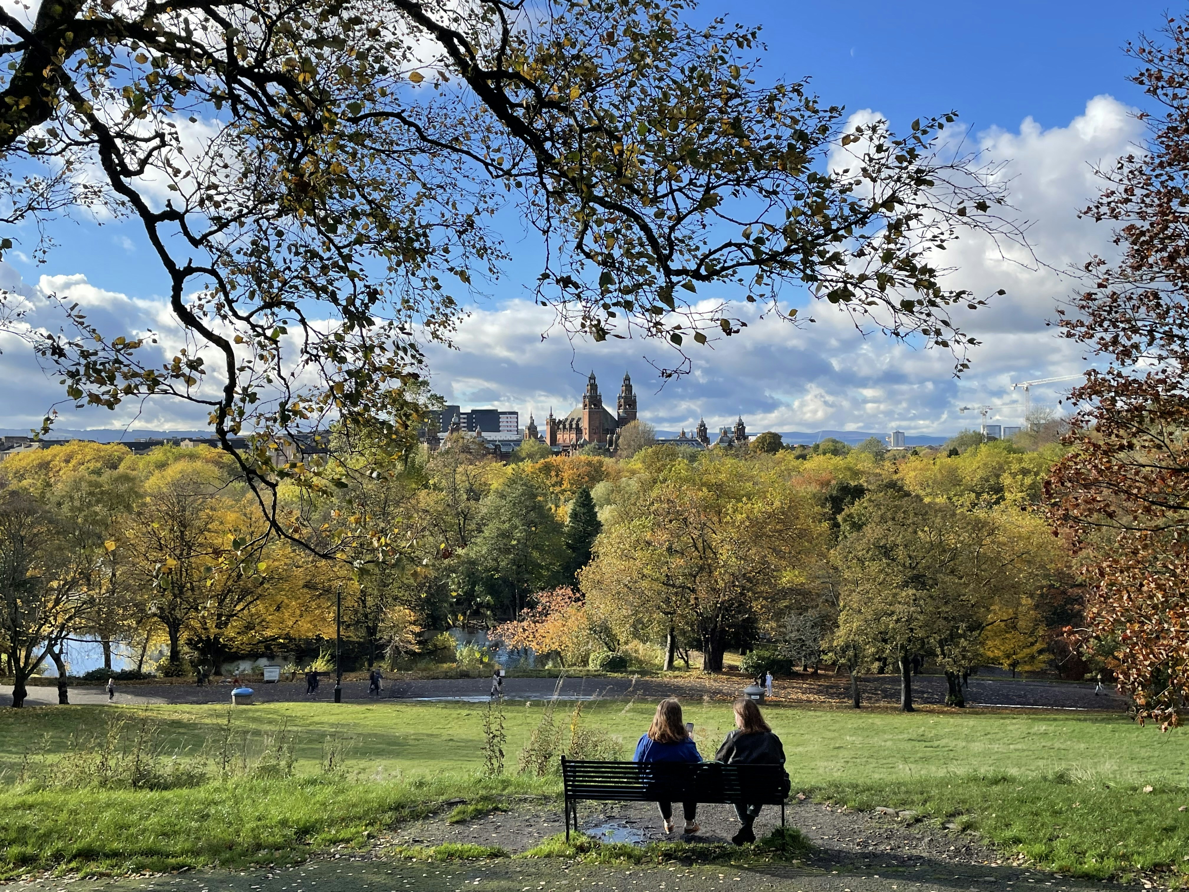 Two people sitting on a bench at night in a quiet city park with soft street lamp glow and autumn leaves