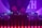 A DJ booth with colorful lights and equipment, including a Denon DJ controller. A person is adjusting the controls, creating a vibrant and dynamic atmosphere with purple and blue hues.