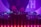 A DJ booth with colorful lights and equipment, including a Denon DJ controller. A person is adjusting the controls, creating a vibrant and dynamic atmosphere with purple and blue hues.