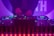 A DJ booth with colorful lights and equipment, including a Denon DJ controller. A person is adjusting the controls, creating a vibrant and dynamic atmosphere with purple and blue hues.
