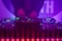 A DJ booth with colorful lights and equipment, including a Denon DJ controller. A person is adjusting the controls, creating a vibrant and dynamic atmosphere with purple and blue hues.
