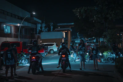 Nighttime gang gathering around roaring motorcycles with flames reflecting off leather jackets.