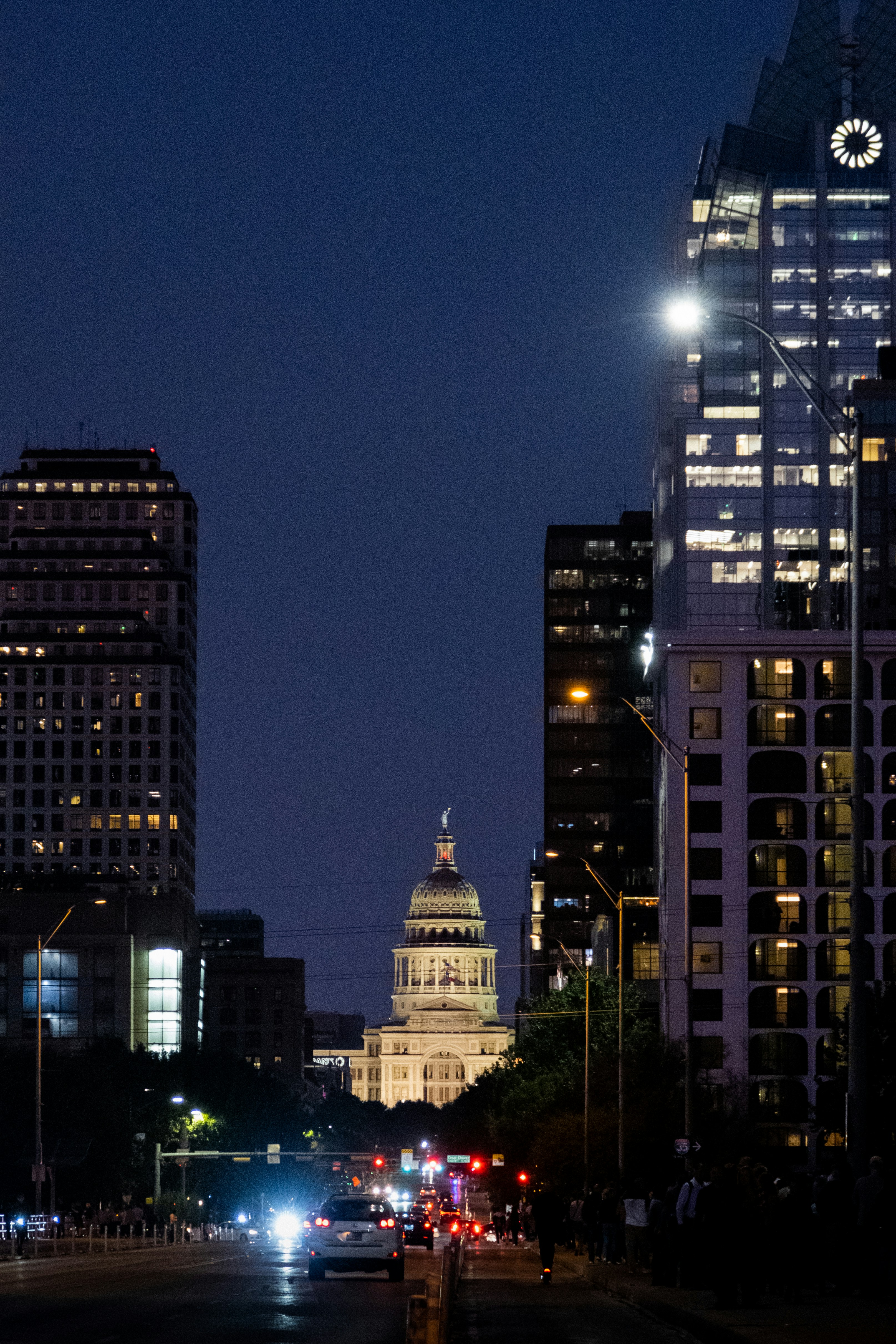 Evening few of a street lined with tall buildings with lit capital dome at the end. 