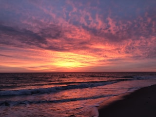 A vibrant sunset over a tropical beach with palm trees and calm waves.