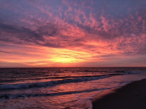 A vibrant sunset over a tropical beach with palm trees and calm waves.