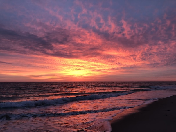 A vibrant sunset over a tranquil beach with gentle waves.