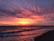 A vibrant sunset over a tropical beach with palm trees and calm waves.