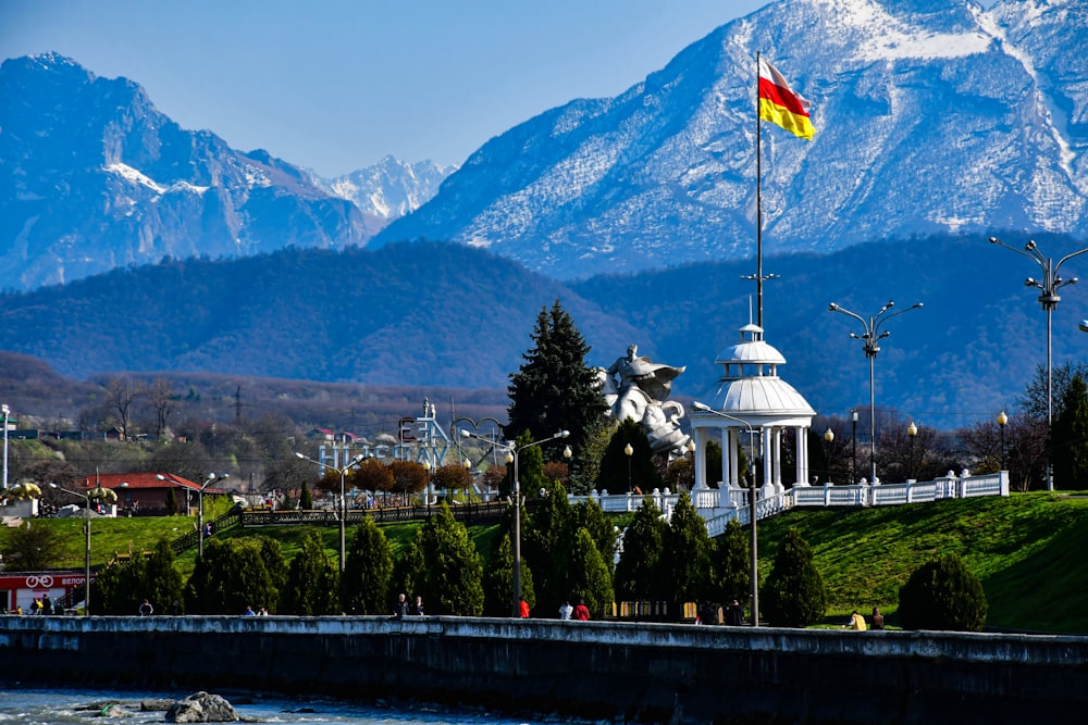 a white building with a flag on top and a statue in front of it with mountains in the