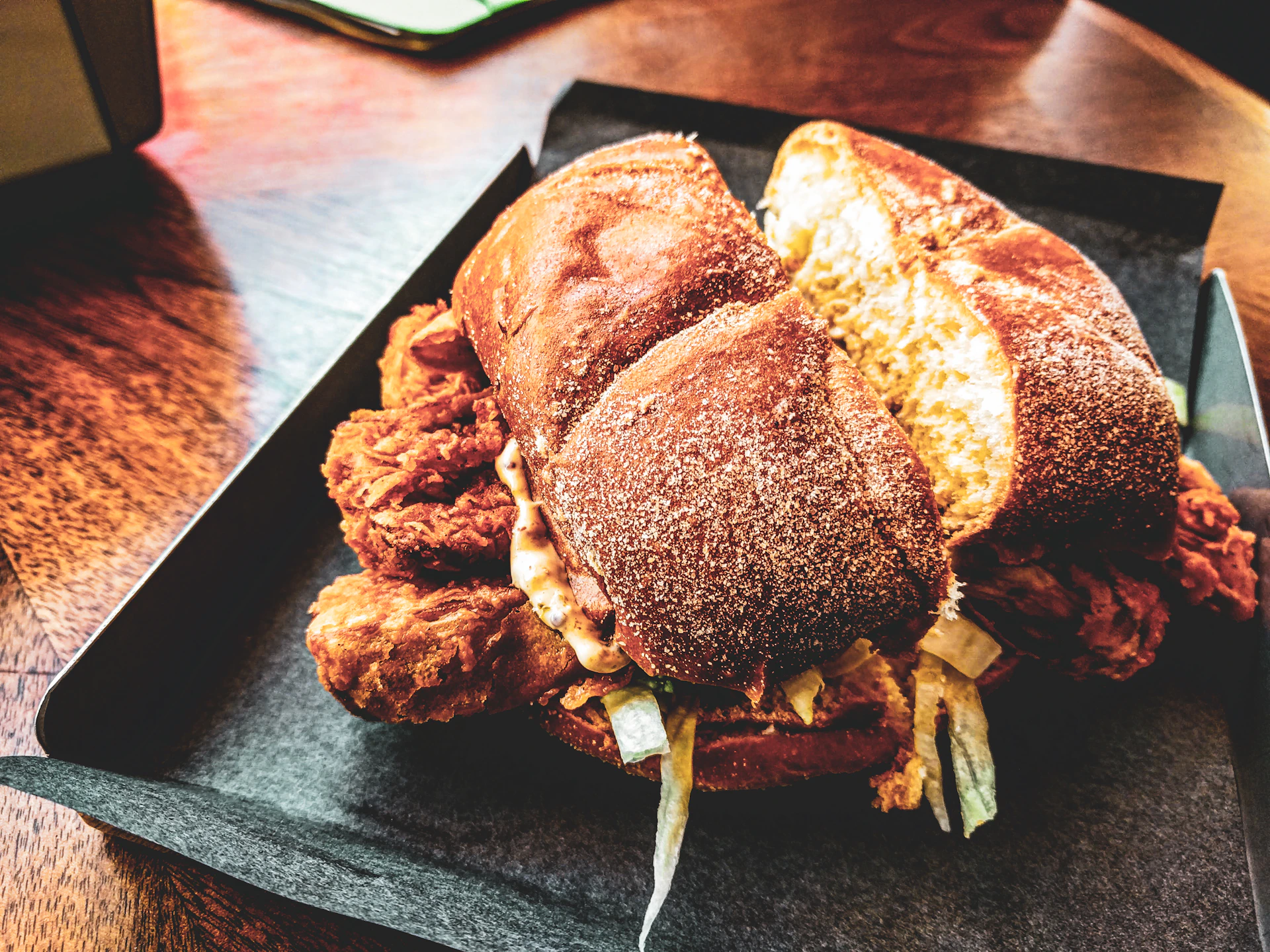 Close-up of a golden, crispy fried chicken sandwich with fresh lettuce and a glossy brioche bun, styled on a black slate plate.