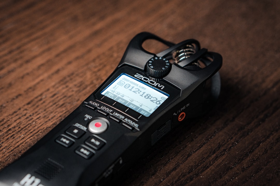 a black phone with a keypad, Zoom h1n audio device, voice recorder laying on the table, recording sounds