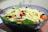A bowl filled with a colorful fresh salad. The salad includes ingredients such as shredded cheese, spinach leaves, chopped carrots, and small pieces of beetroot.
