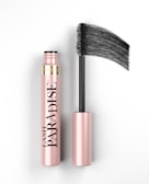 A pink and black mascara tube is displayed with its brush applicator extended, showcasing the brand name 'Lash Paradise' prominently on the tube. The overall look is sleek and elegant with a focus on the product's design.