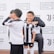 A group of children wearing black and white soccer uniforms are standing on a sports field. One child is smiling broadly, while another makes a playful gesture. They are near a backdrop with the Shanghai American School and Juventus Academy logos.