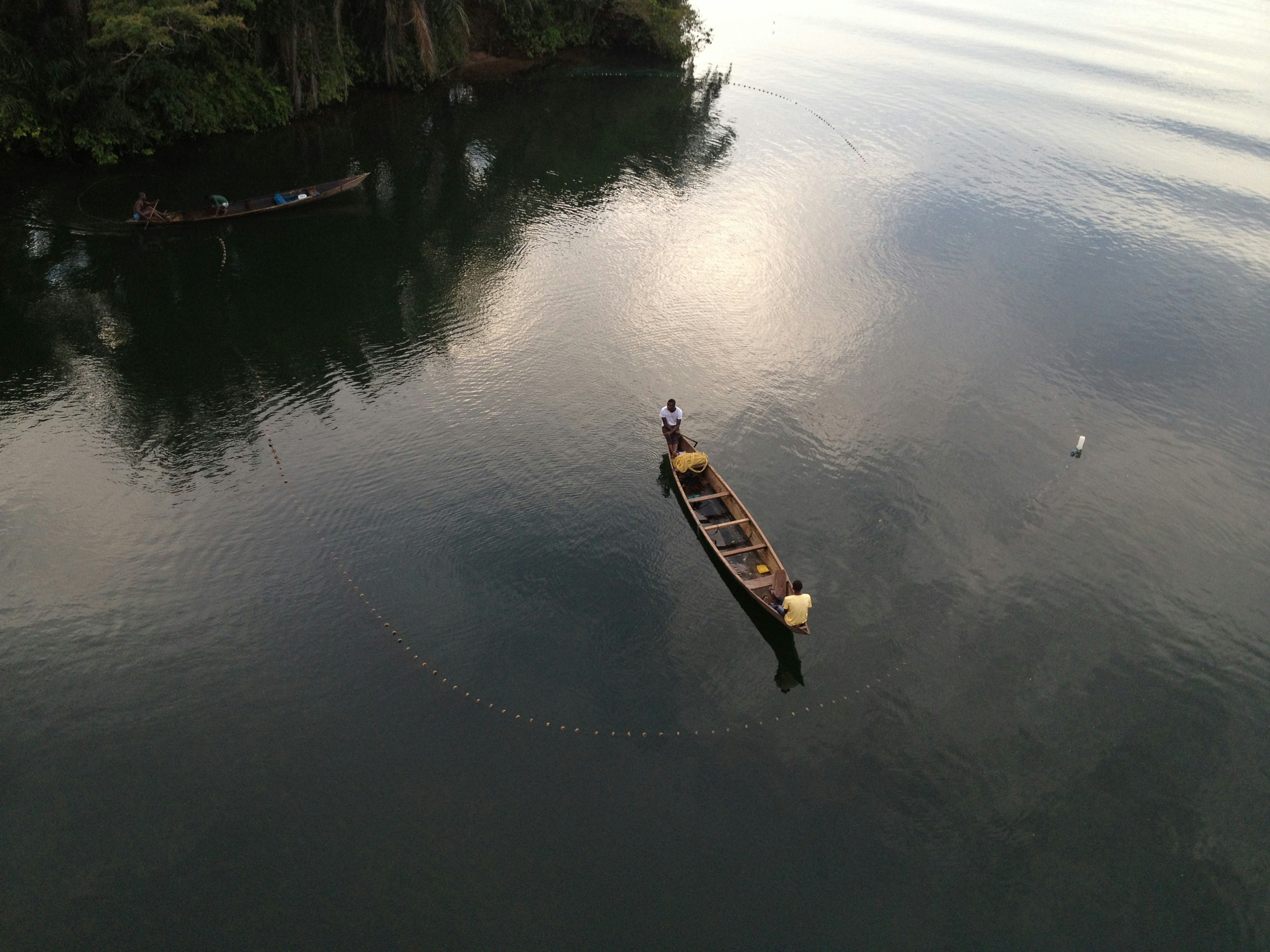 A lone fisherman in a narrow canoe on the dark, still Volta river at Atimpoku, seen from above