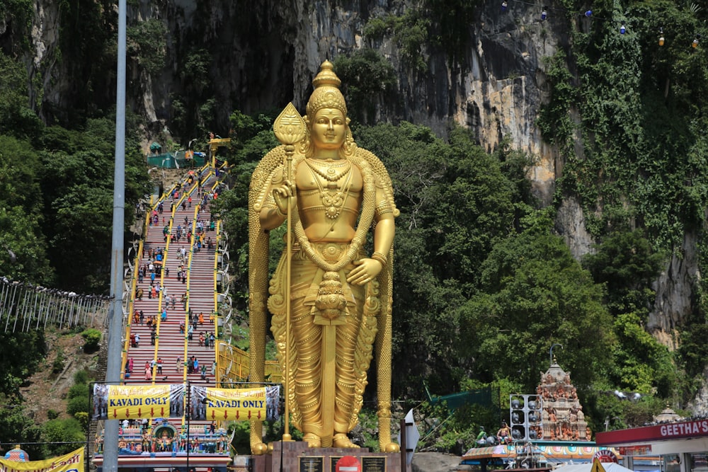 a statue of a person with Batu Caves in the background