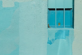 A painter carefully rolling bright turquoise paint onto a living room wall filled with natural light.
