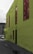 A vibrant green building with large tinted windows stands prominently. The building's exterior features industrial-style lamps mounted along the upper edge. A small portion of a gray concrete alleyway is visible, along with a parked car in the background.