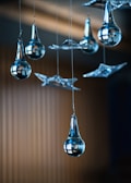 Several glass ornaments, including teardrop-shaped and abstract forms, are hanging from thin wires against a blurred background. The glass is highly polished, reflecting light and the surroundings.