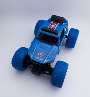 A blue toy monster truck with large textured wheels and a design that includes red and white accents. The top of the truck features a stylized shield emblem, reminiscent of superhero themes, and text that reads 'Captain Regis'.