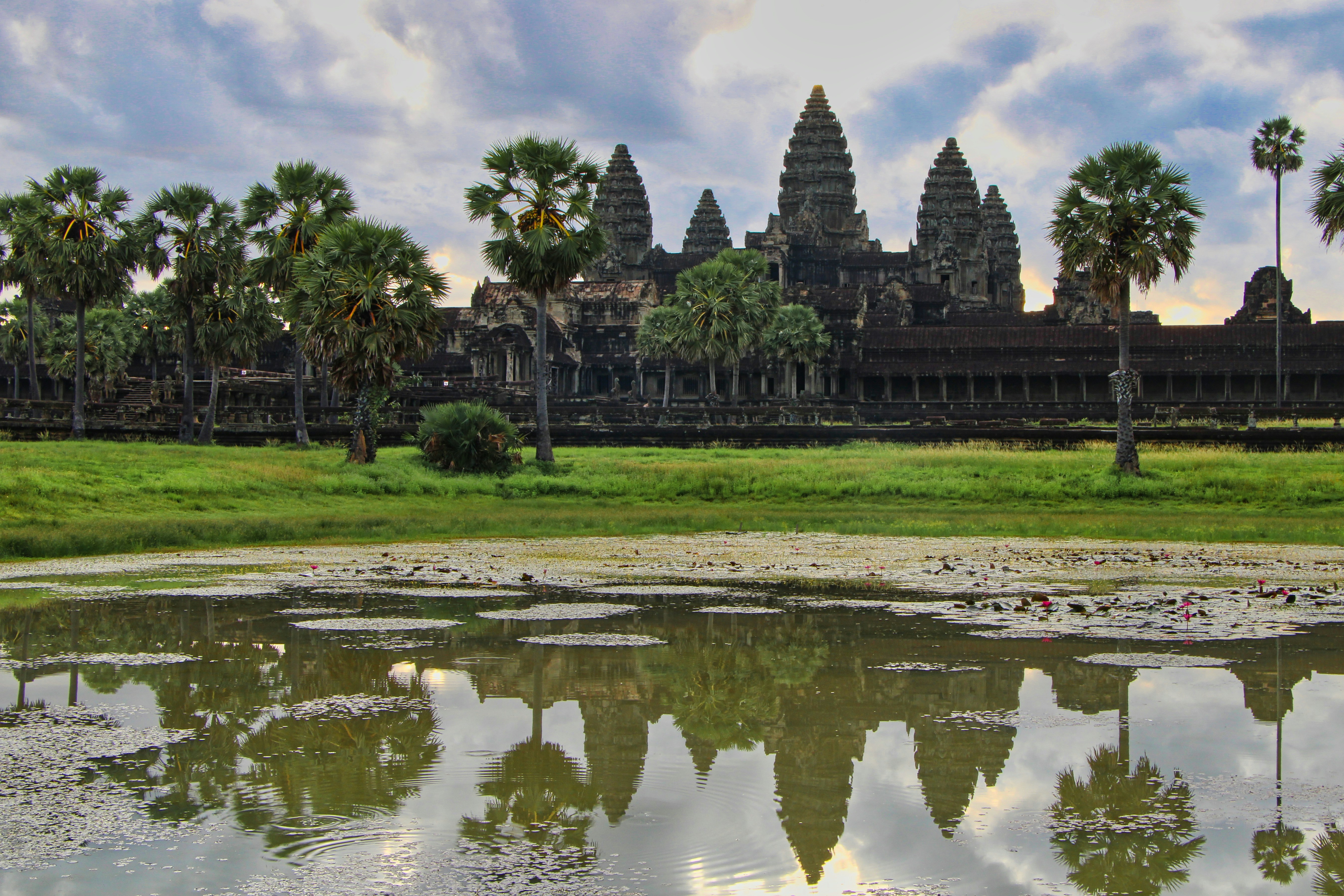 a body of water with trees and buildings in the background with Angkor Wat in the background, The reflection of Angkor Wat on the waterbody