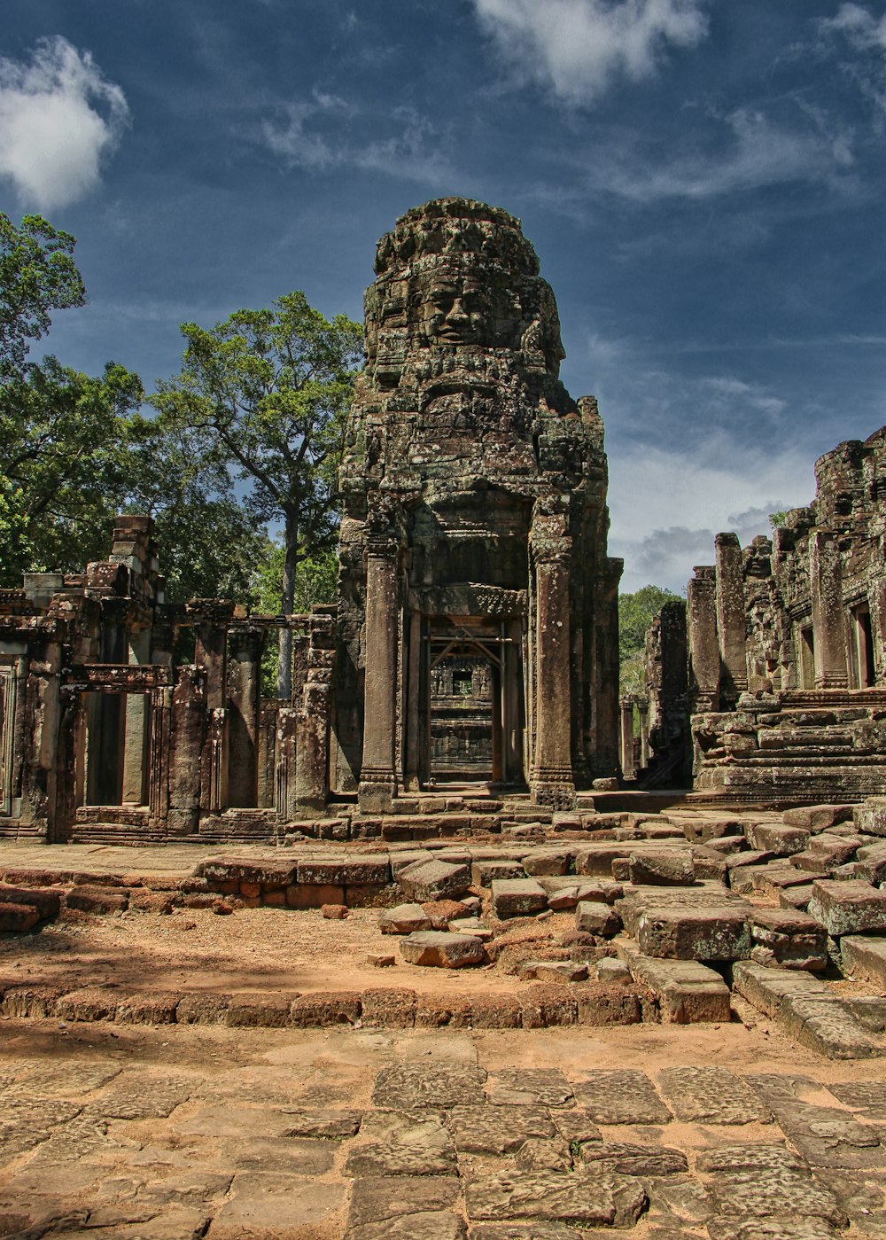 a stone structure with trees and rocks around it with Angkor Wat in the background