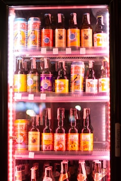 A refrigerator filled with an assortment of bottled and canned beers with colorful labels, neatly arranged on shelves. The labels feature a variety of colors and graphics, including images and text.