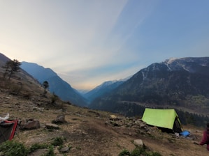 A serene Himalayan tent pitched under a clear blue sky with the Kedarnath mountains in the background.
