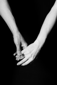 An artistic black-and-white image of hands intertwined, showcasing delicate wedding rings against a minimalist backdrop.