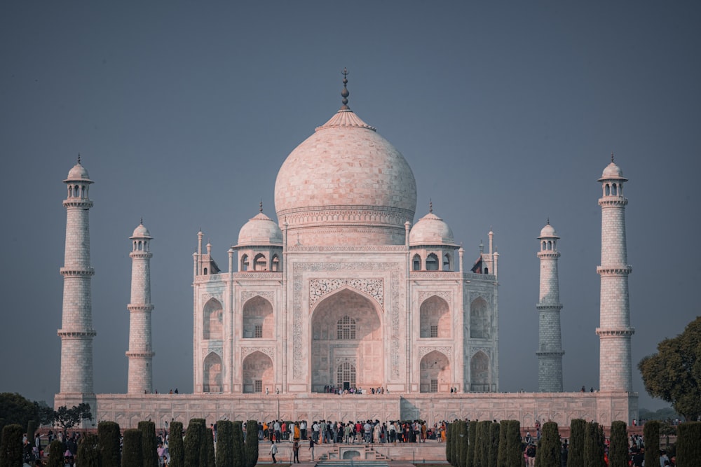 un gran edificio blanco con una cúpula y torres con el Taj Mahal al fondo