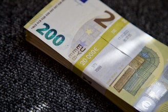 A stack of €200 banknotes is placed on a textured surface. The banknotes are neatly bundled together with a paper band labeled with the amount €20,000. The focus is on the details of the currency, including the watermark and security features.