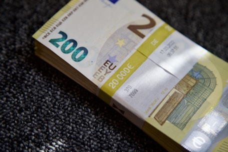 A stack of €200 banknotes is placed on a textured surface. The banknotes are neatly bundled together with a paper band labeled with the amount €20,000. The focus is on the details of the currency, including the watermark and security features.