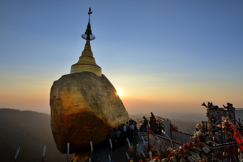 a large rock with a gold top and a gold dome on top with Kyaiktiyo Pagoda in the background