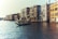 A scenic view of a gondola gliding through a canal in Venice, with grand historical buildings lining the water. The architecture features classic Venetian style with ornate windows and balconies. The water reflects the warm sunlight, creating a peaceful ambiance.