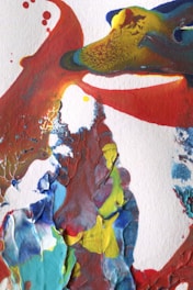 Abstract artwork featuring bold and swirling paint textures in bright colors like red, blue, yellow, and green. The paint appears thick with a mixture of smooth and textured areas, creating a vivid and dynamic composition.