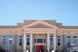 An old brick school building with classic architectural features, including columns and decorative details around the entrance. The facade displays the name 'Ivywild School' above the entrance, with several large windows aligned symmetrically on either side. Two people are visible at the entrance.