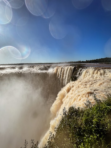a large waterfall with trees and blue sky