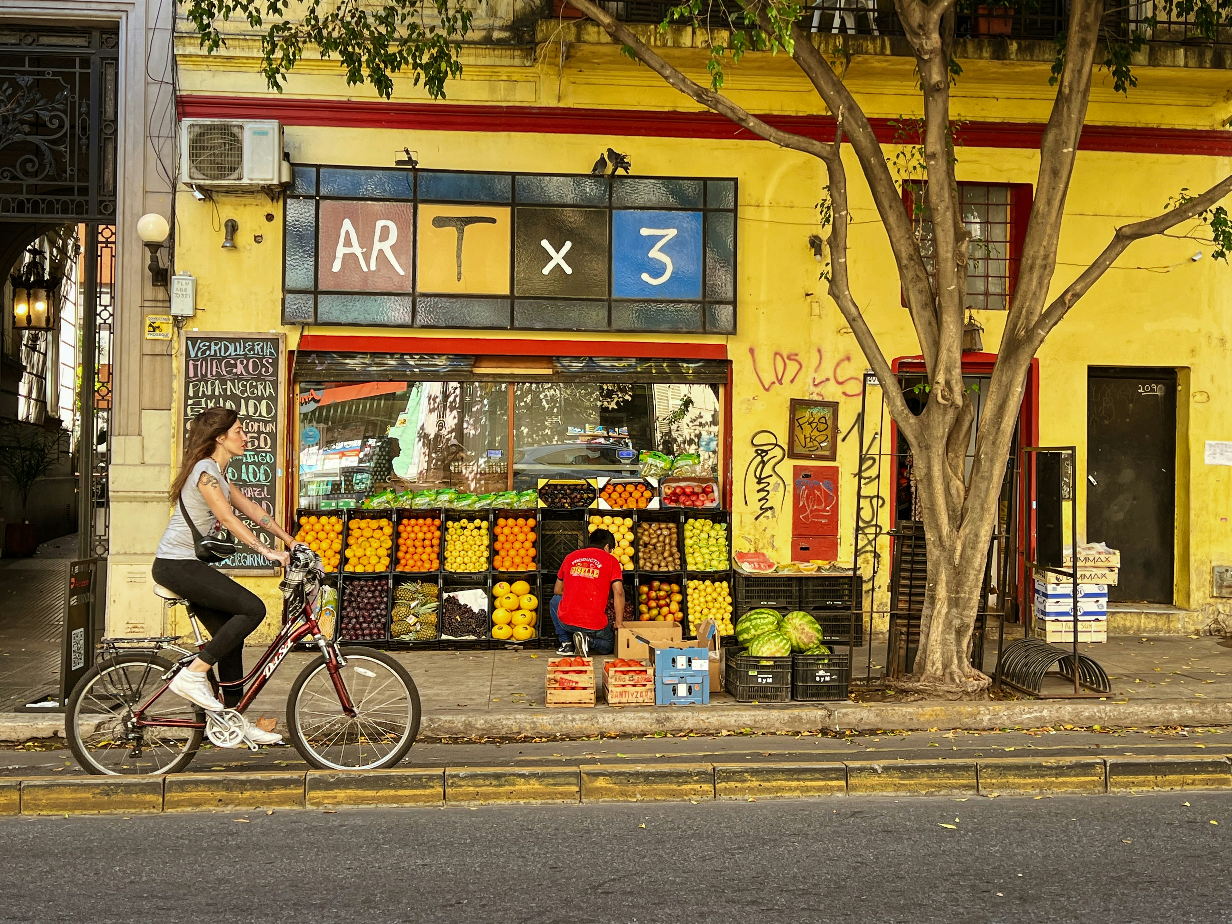 a person riding a bicycle past a fruit stand