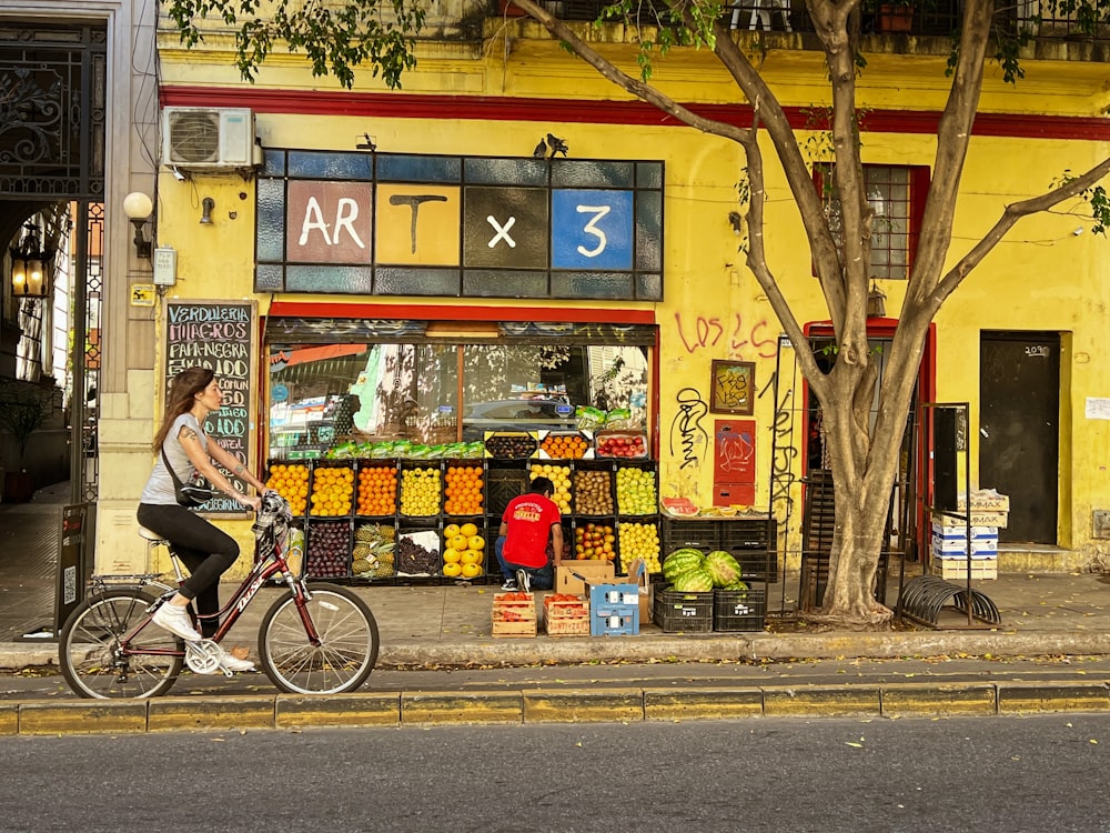 a person riding a bicycle past a fruit stand